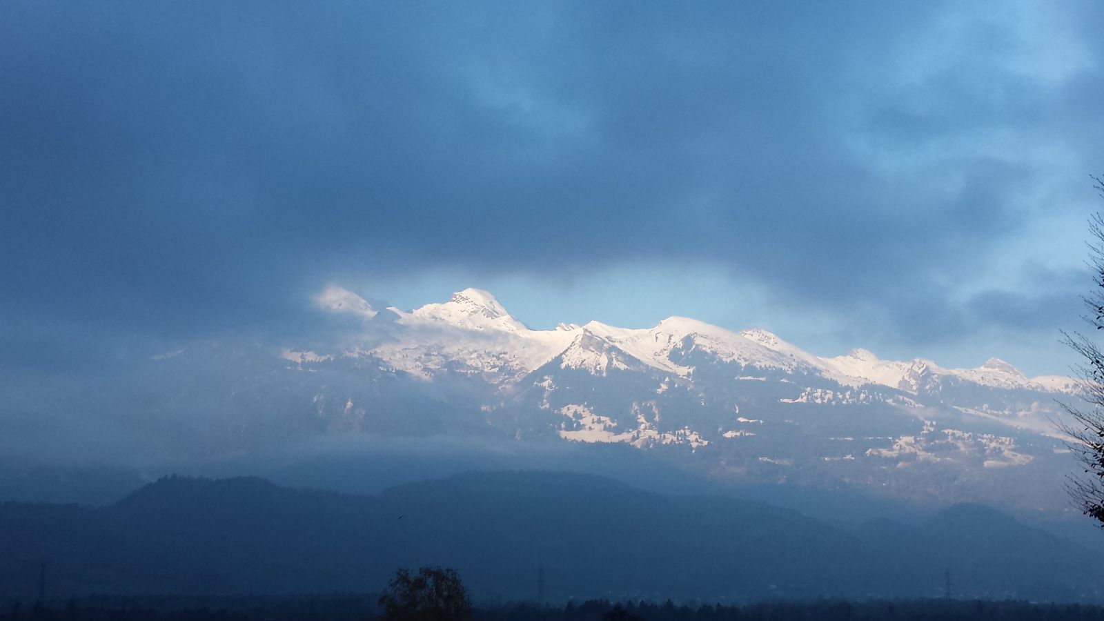 Verschneite Berggipfel unter einem dunklen, wolkigen Himmel.