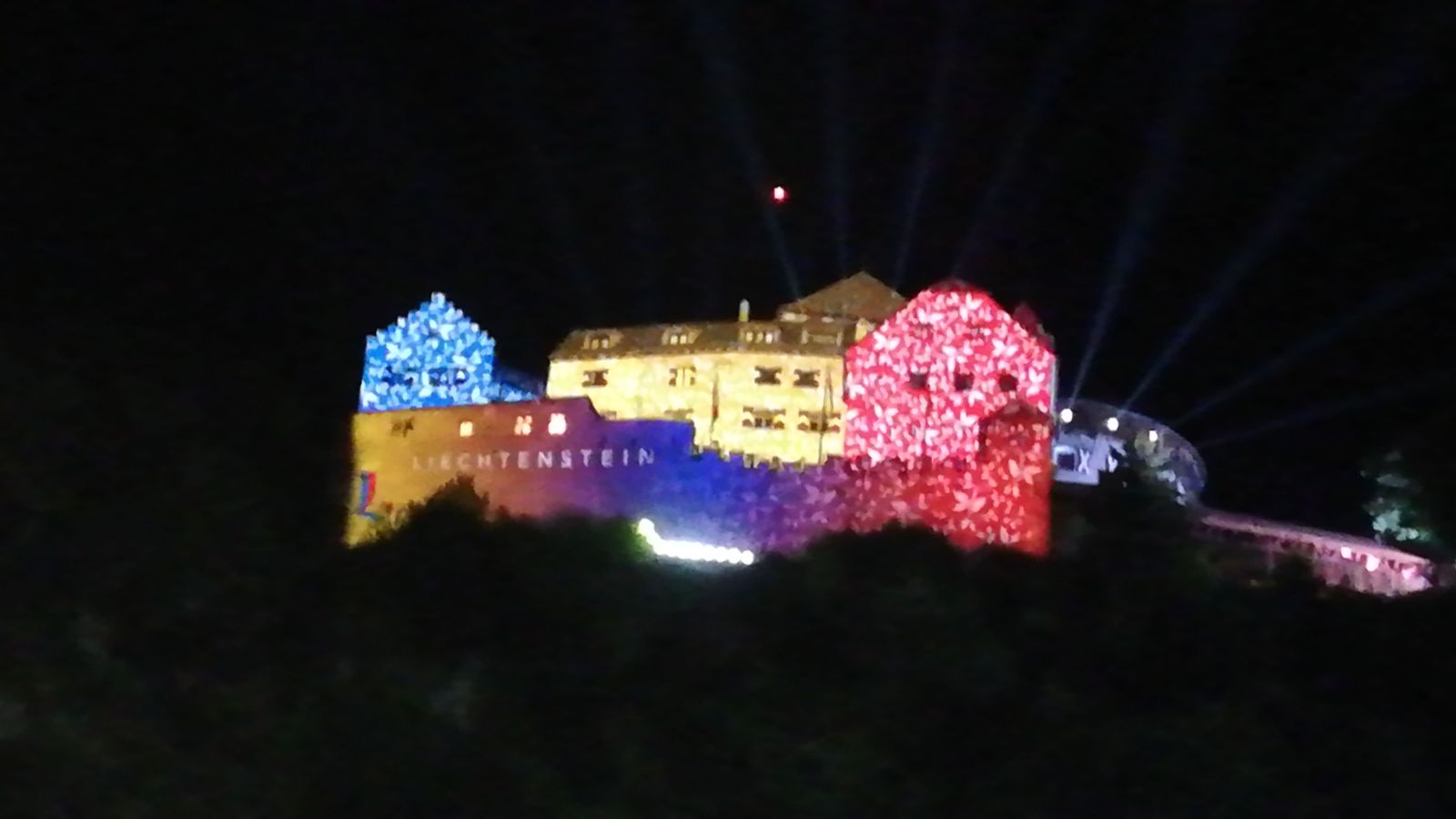 Ein Schloss ist nachts in Blau, Gelb und Rosa beleuchtet.